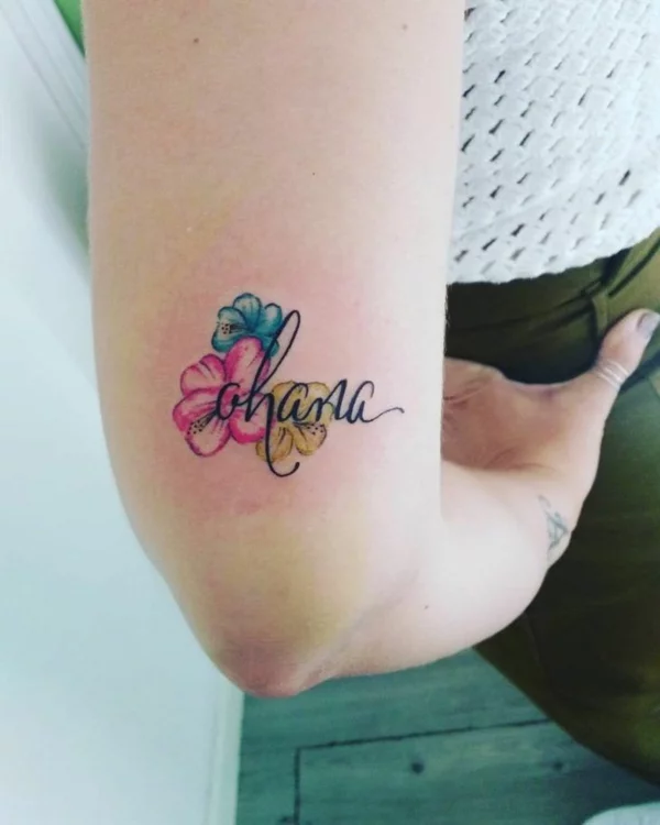 Ohana Schriftzug Tattoo mit bunten Blüten am Oberarm 