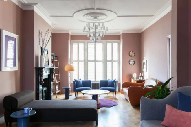 Mid-Century Modern Wohnstil Wohnzimmer rosafarbene Wände bequeme Möbel Kamin aus Stein violetter Teppich