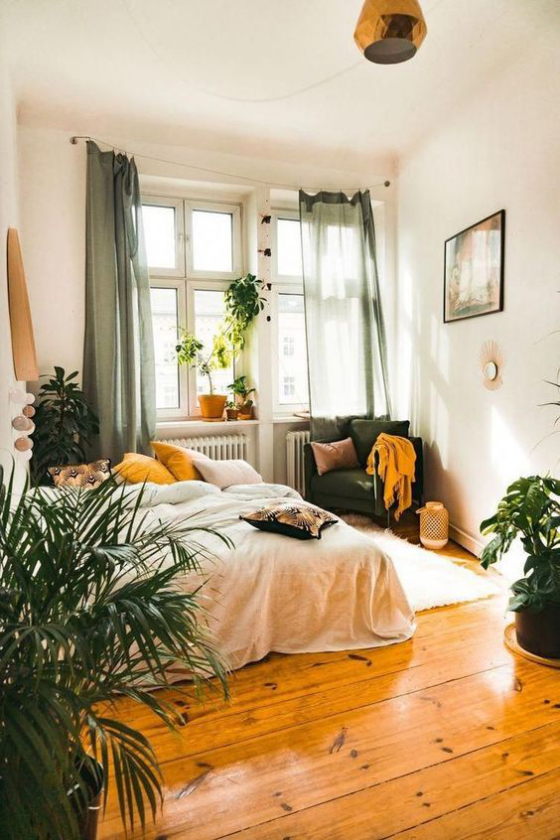 kleines Schlafzimmer Holzboden viele grüne Pflanzen Bett in Grün gebettet Sessel in der Ecke neben dem Fenster Akzente in Gelb