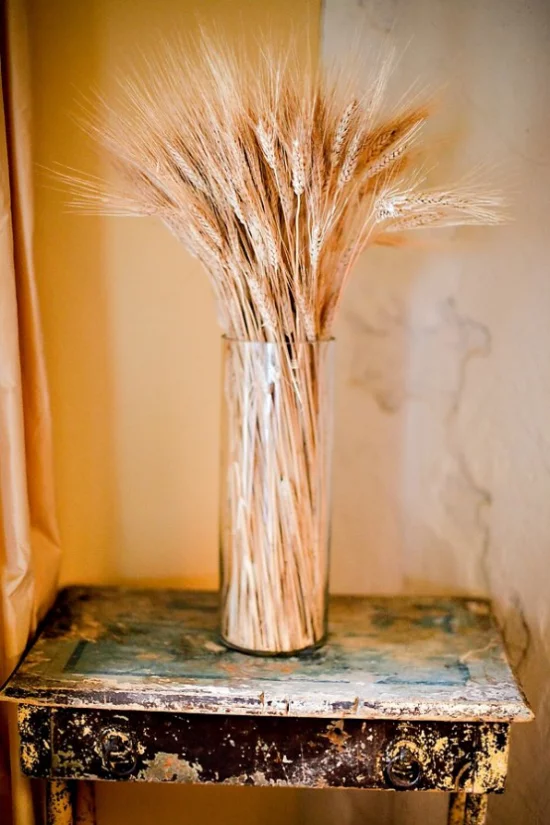 Herbstdeko mit Weizen hohe Vase aus Glas Weizenstängel darin arrangiert Vintage Tisch in einer Zimmerecke