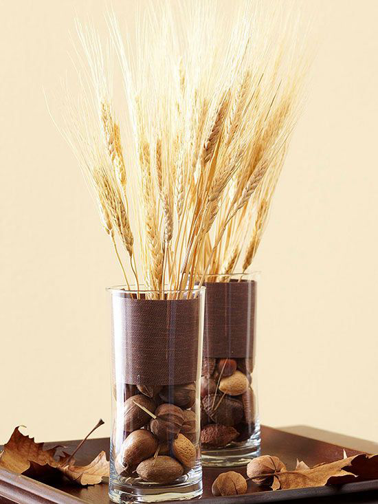 Herbstdeko mit Weizen zwei elegante Vasen aus Glas Weizenstängel Nüsse Herbstblätter auf Holztablett