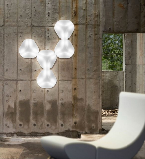 Extravagante Wandleuchten Industrial Style grobe graue Betonwand fünf Lampen gruppiert geometrische Form schicker Sessel im Vordergrund