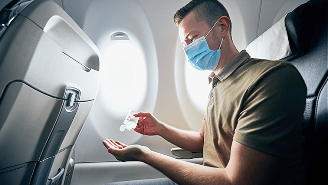 Fliegen während Corona Passagier im Flugzeug Desinfektionsmittel benutzen Hände desinfizieren