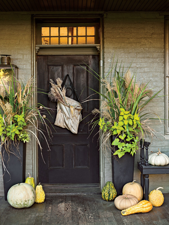 Herbstdeko für draußen im rustikalen Stil Beutel mit getrockneten Gräsern dunkle Tür zwei hohen Blumenbehälter beiderseits Kürbisse verschiedene Farben und Größen