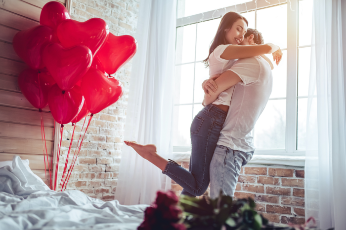 Verliebt sein Sternzeichen zum Valentinstag rote Ballons rote Rosen glücklich sein junges Paar im Schlafzimmer