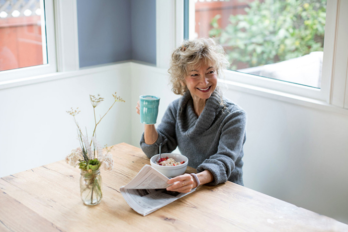Abnehmen im Alter Frau allein beim Frühstück kleine Portion Tee trinken Zeitung lesen