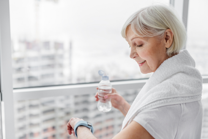 Abnehmen im Alter Frau beim aktiven Sporttreiben viel Wasser trinken den Pulsschlag und Blutdruck kontrollieren