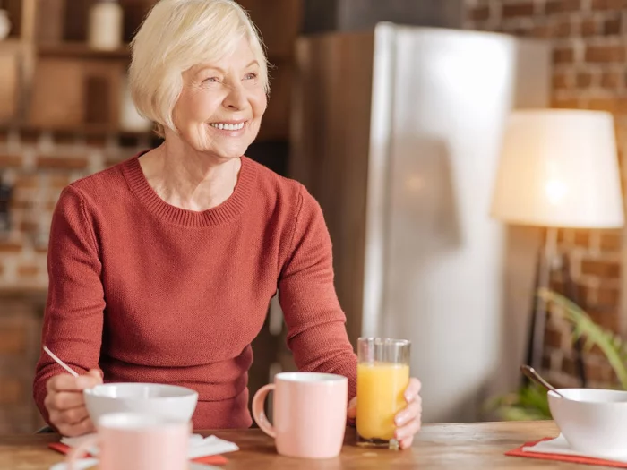 Abnehmen im Alter ältere Frau in der Küche schreibt etwas auf trinkt Smoothie Tee