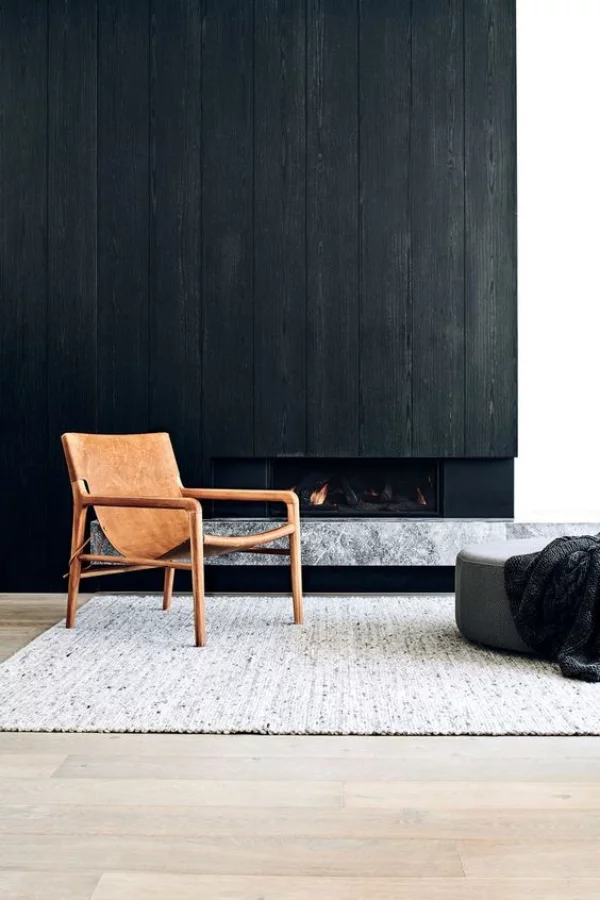 Schwarze Wand Wohnzimmer Kamin ein Stuhl vor dem dunklen Hintergrund grauer Hocker Teppich