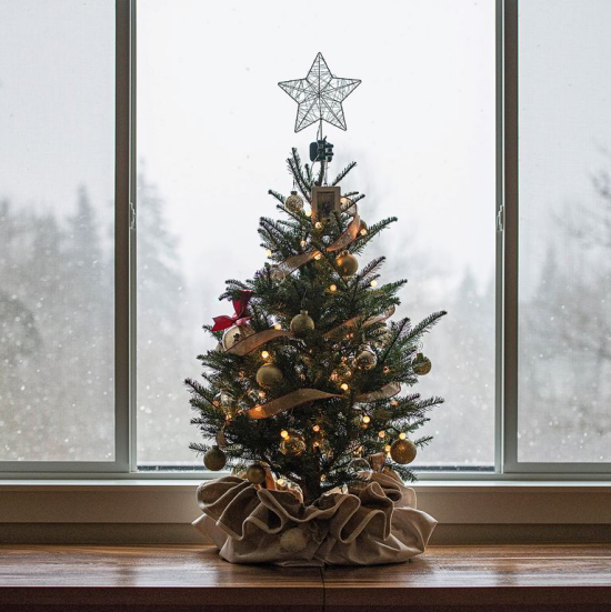 Weihnachtliche Fensterdeko ein kleiner stilvoll geschmückter Christbaum im Topf Leinensack Stern goldglitzernde Kugeln