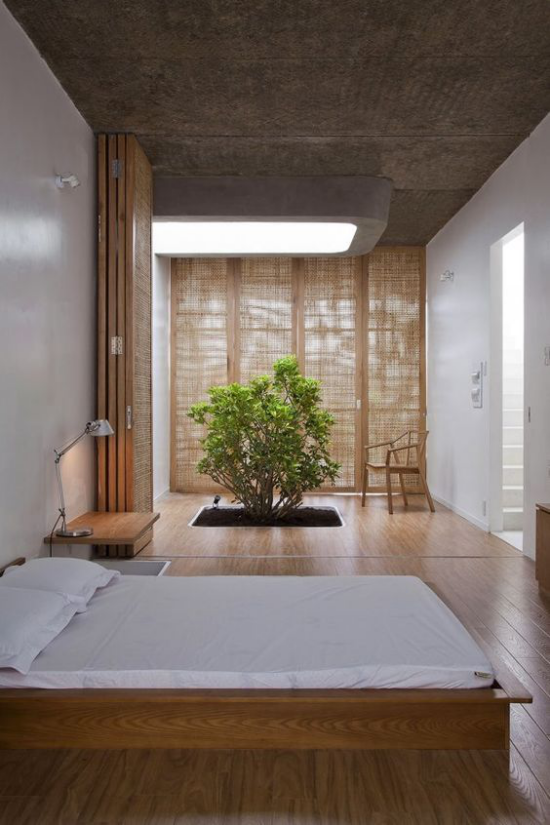 Zen Schlafzimmer weites Schlafbett helle Bettwäsche viel Holz großes abgedunkeltes Fenster ein kleiner Baum grüne Note