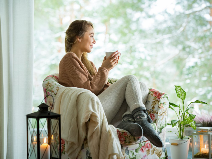 gesund und glücklich im Winter bleiben gemütlich machen zu Hause Frau im Sessel Tee trinken Relax eine grüne Pflanze daneben