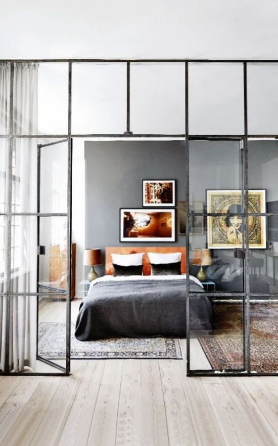 Glaswände im Schlafzimmer schwarzer Metallrahmen zwei bunte Teppiche interessante Wandbilder sehr einladend