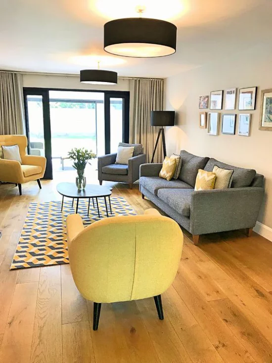 Trendfarben 2021 im Interieur schickes geräumiges Wohnzimmer graue Couch ein grauer Sessel zwei gelbe Sessel sehr einladend