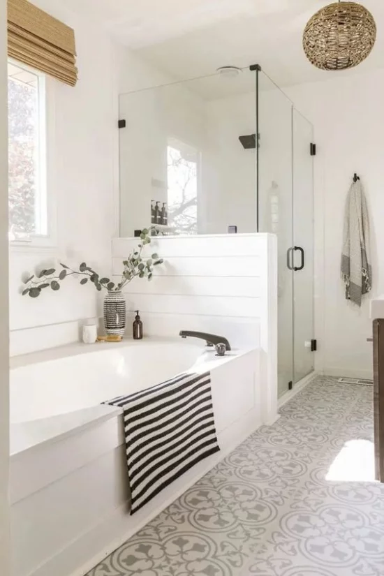 Badezimmer Trends 2021 weiße Badewannen Duschecke daneben Glastür leicht gemusterte Bodenfliesen Badetuch in schwarz-weißen Streifen