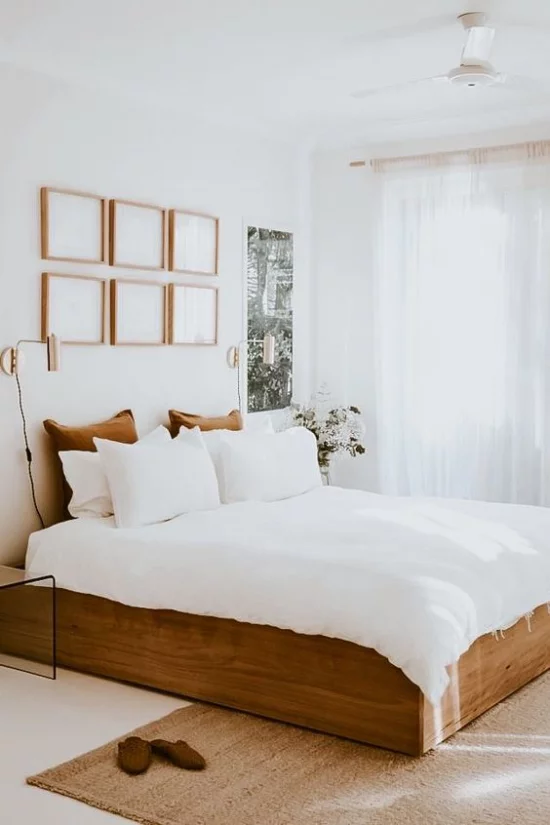 kleines Schlafzimmer optisch erweitern Schlafbett aus Holz weiße Bettwäsche Kissen Wanddekoration Fenster viel Licht