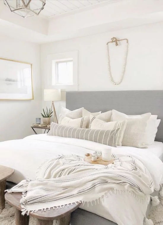 kleines Schlafzimmer optisch erweitern helle Bettwäsche Tagesdecke aus Wolle graues Bettkopfteil viele Deko Kissen