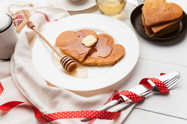 romantisches Frühstück zu zweit Pfannkuchen in Herzform mit Butter und Honig