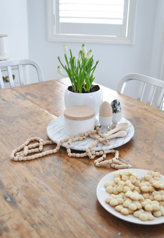 skandinavische Frühlingsdeko Tisch aus hellem Holz weiße Blumen im Topf andere Deko Artikel