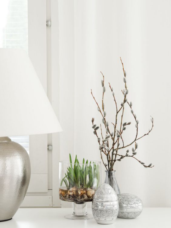 skandinavische Frühlingsdeko Tischdeko neben Tischlampe Eier Vase mit Zweigen Glasgefäß mit Frühlingsblumen