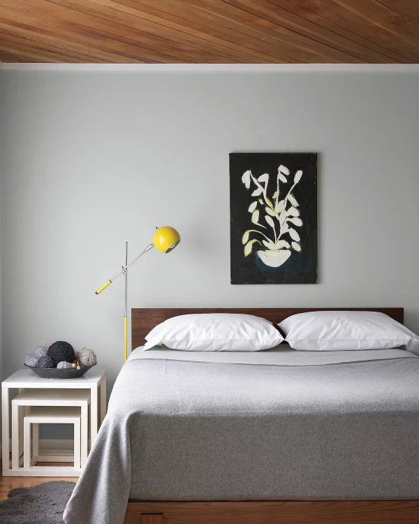 Aktuelle Wandfarben graues Schlafzimmer Hellgrau an der Wand Tagesdecke weiße Kissen kleines Highlight in Gelb Lampe