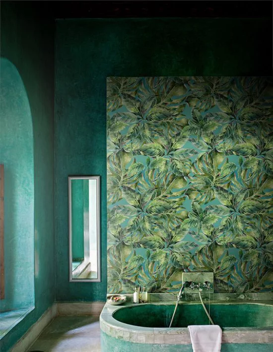 Tropische Deko im Bad grüne Wände Tapete exotische Blätter eingebaute Badewanne Wandspiegel im Hintergrund Fenster links