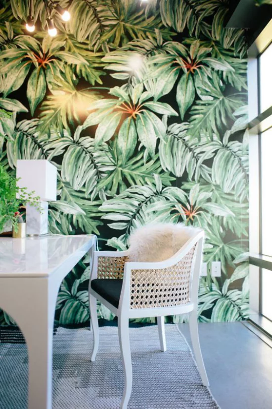 Tropische Deko im Home Office weiße Möbel Akzentwand große tropische Blätter auf Tapete schicke Beleuchtung viel Tageslicht