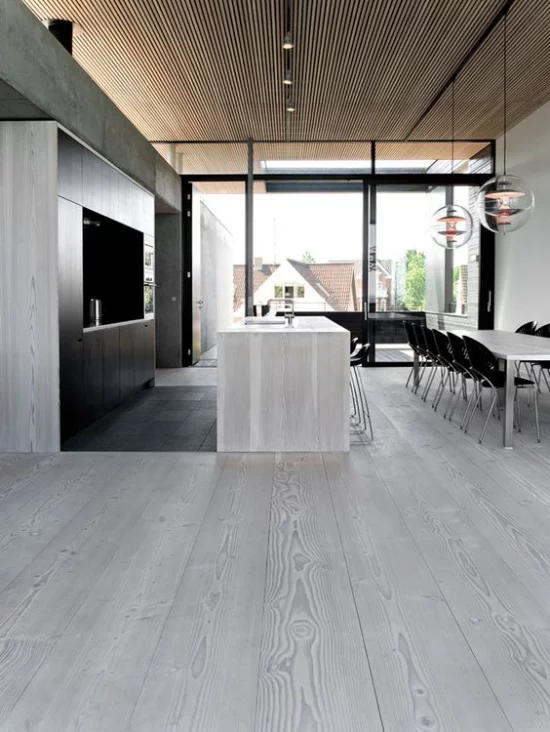 grauer Boden geräumige sehr moderne Küche mit Kücheninsel Esstisch Essecke daneben sehr schlichte Raumgestaltung