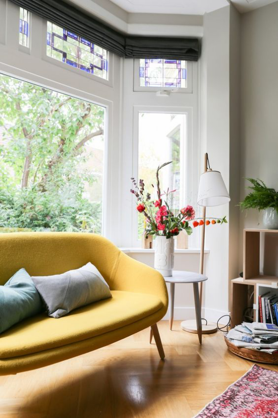 Erkerfenster Wohnzimmer gelbes Sofa Kissen kleiner Tisch Vase mit Blumen Bücherregal Teppich