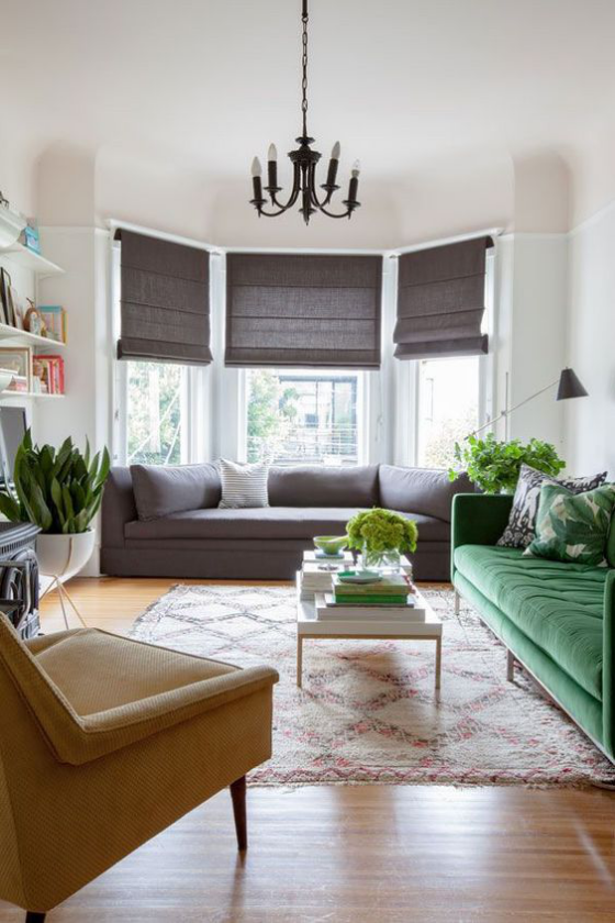 Erkerfenster im Wohnzimmer zusätzliche Wohnfläche dunkle Faltrollos bequeme Sofas Sessel Teppich grüne Zimmerpflanzen