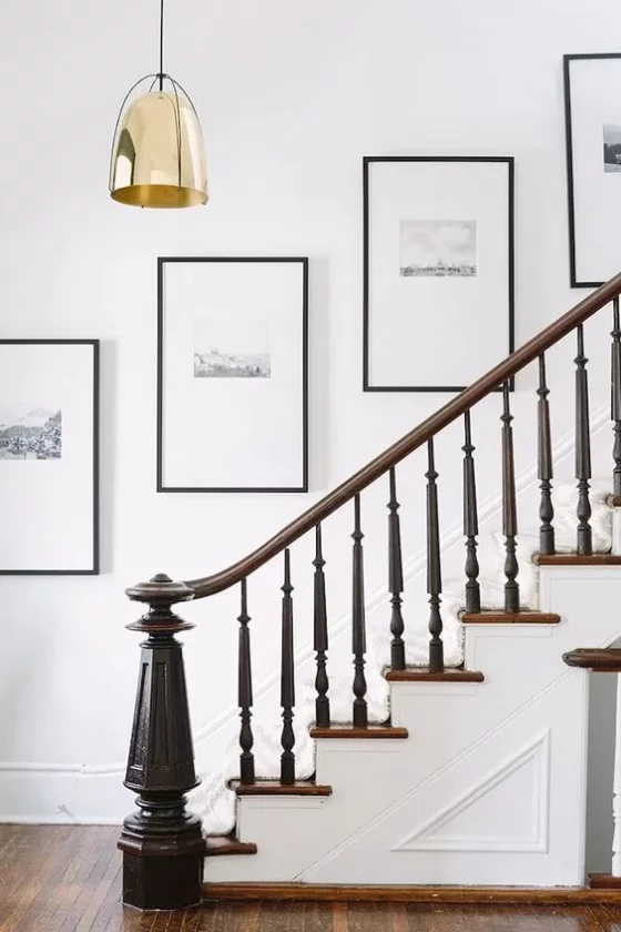 Fotowand im Treppenhaus symmetrische Hängung einer Linie entlang angeordnet kleine Bilder weißer Hintergrund dünne schwarze Rahmen