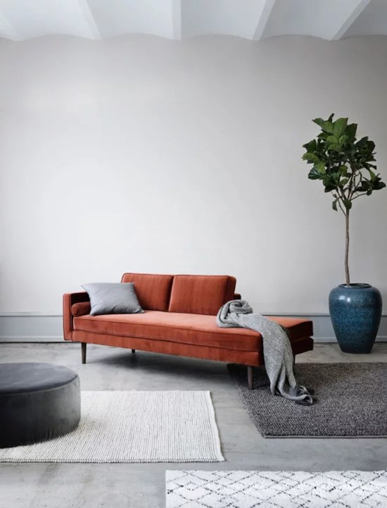 Mehr Farbe ins Interieur graues Wohnzimmer Sofa in Orange graue Wurfdecke Teppiche Grünpflanze im Topf