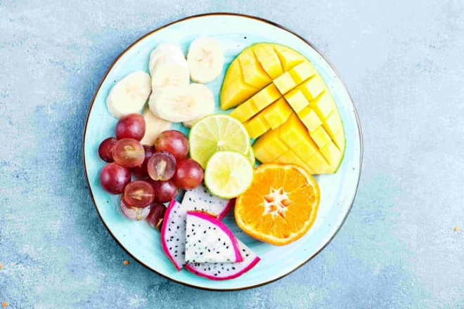 Obst essen gesund abnehmen abends Früchte meiden auf einem Teller Ananas Orangen Banane in Scheiben geschnitten Trauben