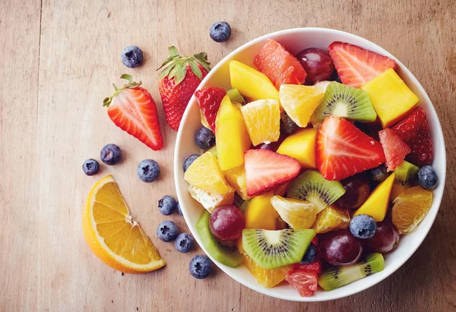 Obst essen gesund abnehmen reichhaltiger Obstsalat Orangen Kiwi Erdbeeren Blaubeeren in Stücke geschnitten in einer Schüssel.