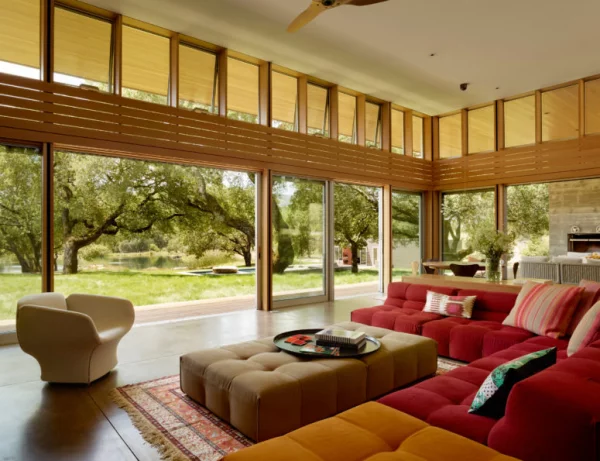 Open-Air-Wohnzimmer hohe Glaswände bequeme Sitzmöbel warme Farben Blick auf den Garten viel Grün draußen