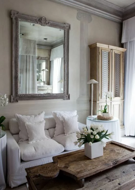Provence-Stil gemütliches Wohnzimmer romantische Raumgestaltung bequeme Möbel weiße Bezüge Kissen Holztisch weiße Tulpen Wandspiegel