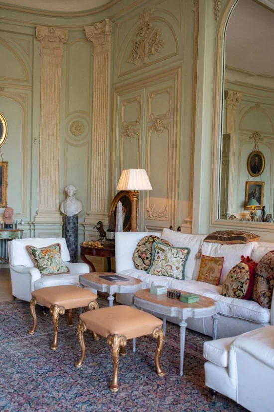 Provence-Stil klassische Einrichtung im Wohnzimmer weiße Sitzmöbel gemusterte Wurfkissen zwei kleine Tische zwei Hocker Lampe