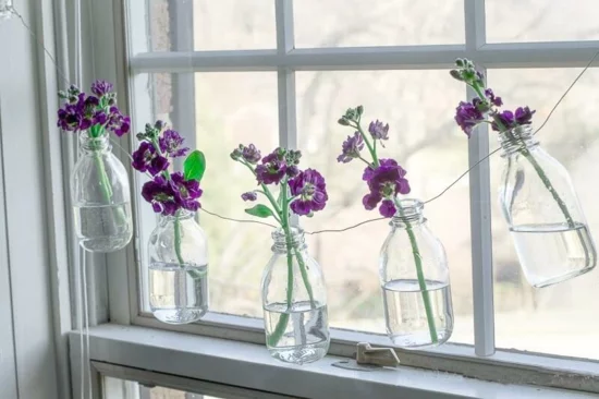 Fensterdeko aus Glasflaschen voller Blumen 