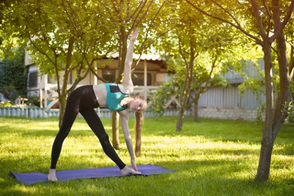 Yoga Garten anlegen und gestalten junges Mädchen macht Yoga Übungen im Schatten hoher Bäume im Freien