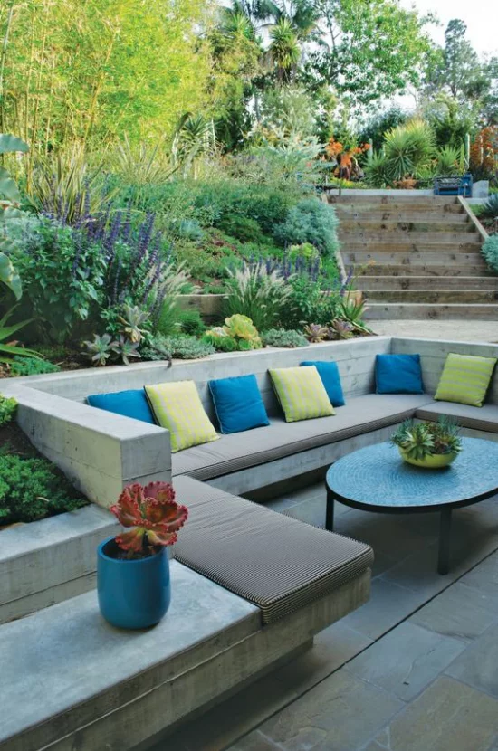 versunkener Sitzbereich im Freien interessante Gestaltung einzelne Zonen abgetrennt gelbe und blaue Kissen Polsterung viele Grünpflanzen