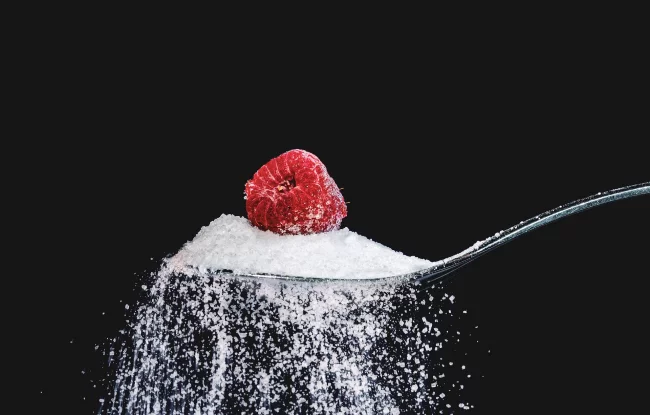 Diätfallen frisches Obst essen ohne Zucker eine Himbeere auf einem Haufen Zucker lecker aber ungesund