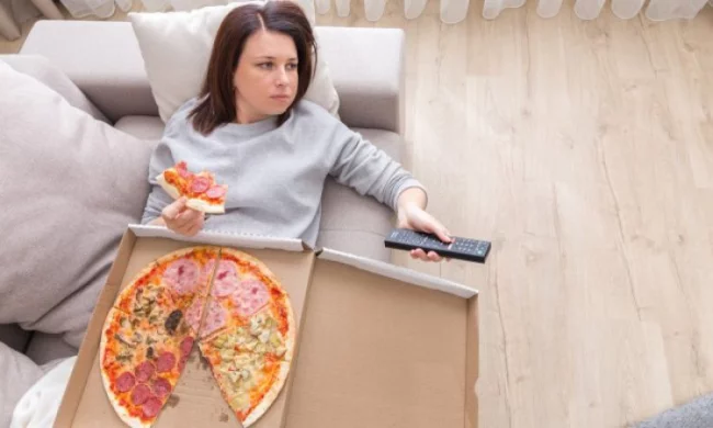 Diätfallen  junge Frau liegt auf der Couch vor dem Fernseher isst Pizza schlechte Gewohnheit