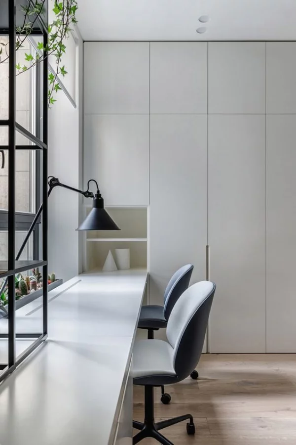 minimalistisches Home-Office viel Tageslicht langer Tisch vor dem Fenster Grau dominiert Schreibtischlampe