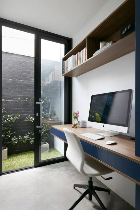 zeitgenössisches Home Office große Glastür Blick zum Innenhof langer Schreibtisch PC weißer Sessel Regal