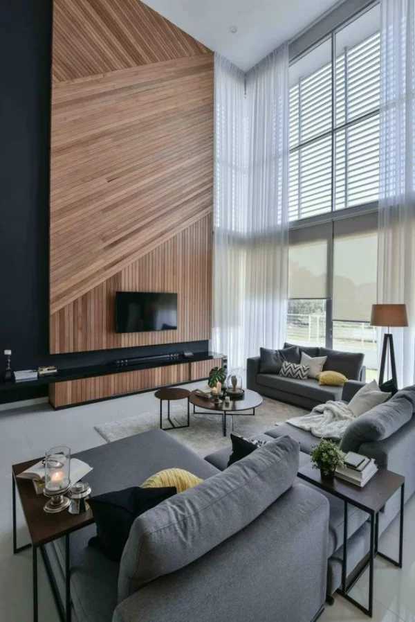 modernes Wohnzimmer auf zwei Ebenen Holzwand als Blickfang graue Sitzmöbel Kissen Tische Kerzen einladend und gemütlich wirken