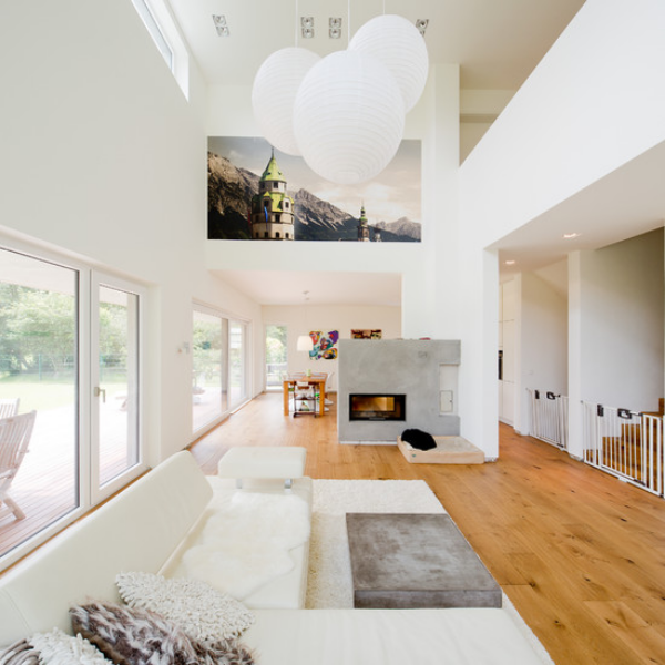 modernes Wohnzimmer auf zwei Ebenen schicke Raumgestaltung in Weiß Hängeleuchten Wandbild helles Holz auf dem Boden Betonwand mit Kamin