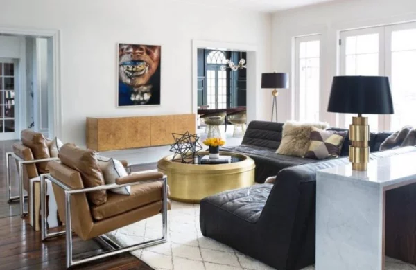 modernes Wohnzimmer eklektisches Raumdesign Ledersessel schwarzes Ledersofa goldglänzender runder Tisch in der Mitte Wandbilder zu viele Farben