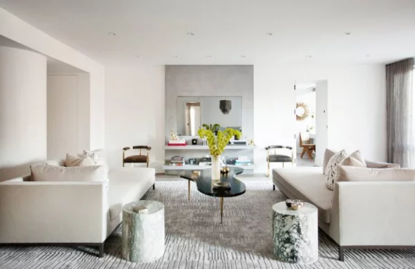 modernes Wohnzimmer geometrische Formen helle Farben zwei Sofas Teppich kleiner schwarzer Kaffeetisch zwei Baumstammhocker