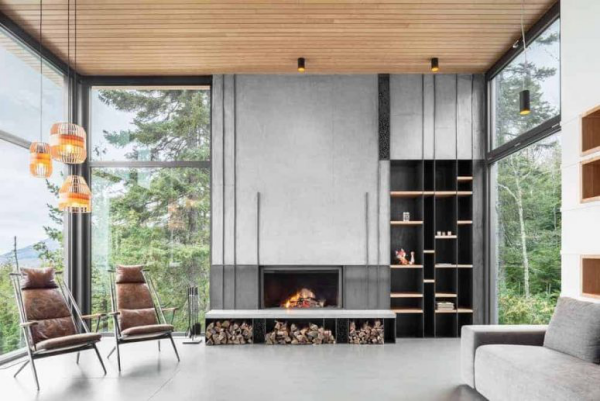 modernes Wohnzimmer sauberes Ambiente wenige Möbel Kamin Brennholz zwei Sessel deckenhohe Fenster Blick auf die Natur
