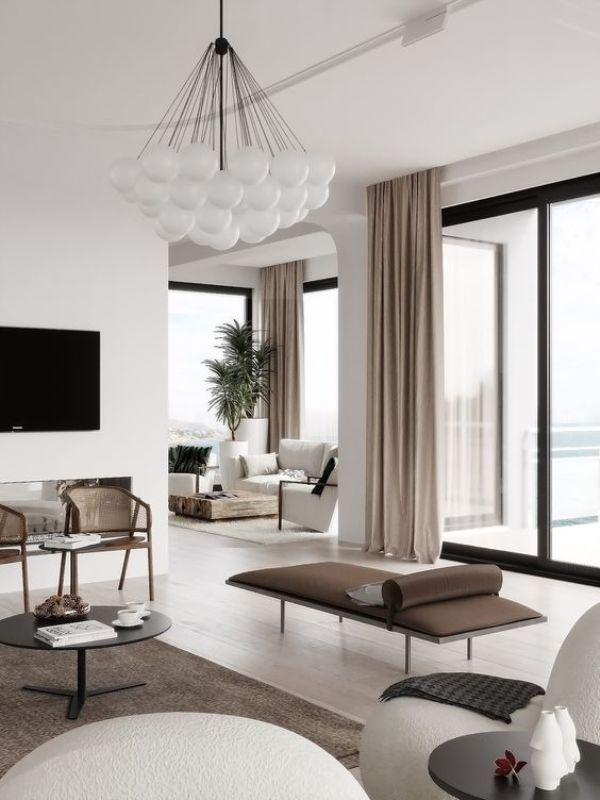modernes Wohnzimmer weiß grau taupe interessante Möbelanordnung viel Luft im Raum hellbraune Fenstergardinen schicker Kronleuchter grüne Topfpflanze im Hintergrund
